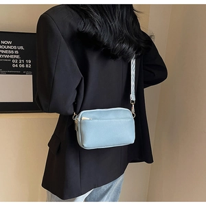 Detail of light blue crossbody bag featuring a textured geometric pattern fabric strap