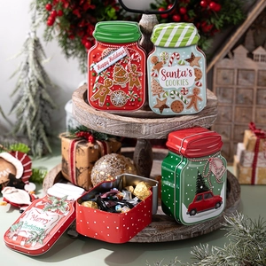 Christmas mason-style tin cookie jars with festive prints on a wooden display tray