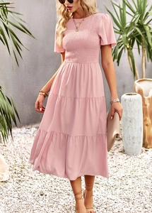 Pink tiered midi dress with smocked waist detail and short sleeves in outdoor garden