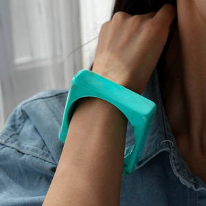 Close-up of wide square turquoise resin bangle on denim sleeve showing polished finish