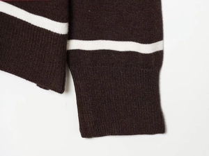 Detailaufnahme des dunkelbraunen Strickärmels mit weißem Streifen und Rippbündchen