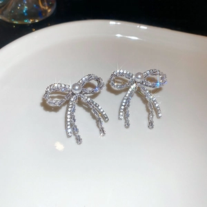 Detailed view of silver bow earrings with sparkling zircons and a white round pearl
