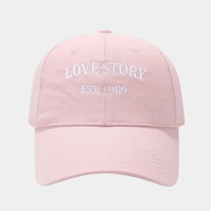 Detail showing the intricate white LOVE STORY embroidery on pink cotton baseball cap