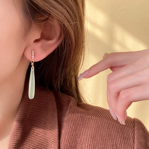 Close-up of gold pear-cut green jade earrings with sparkling zircon accents on a model