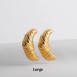 Macro detail of large gold croissant earrings with polished metal texture and spiral pattern