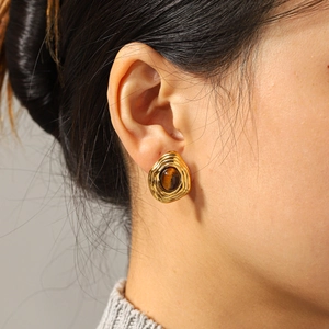 Close-up of vintage gold wavy earrings with brown tiger eye stone on a model