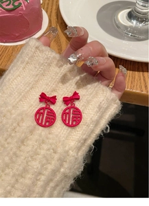 Macro shot of red Fu character bow earrings on a cream knit sweater sleeve