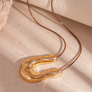 Detailed close-up of golden U-shaped liquid metal pendant on a brown cord necklace