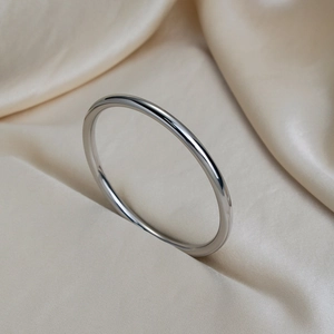 Polished silver stainless steel bangle bracelet on beige silk fabric background