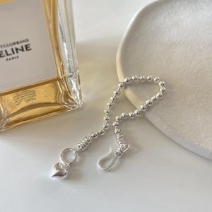 Close-up of a silver beaded bracelet with heart pendant on a white ceramic tray