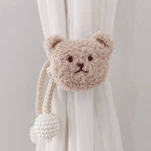 Close-up of beige plush bear curtain tieback with pearl bead detail on white drapes