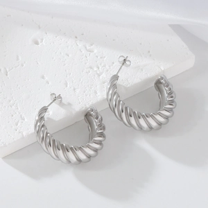 Polished silver croissant hoop earrings in stainless steel on white textured stone background