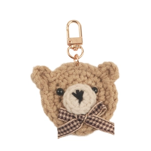 Cute brown hand-knitted crochet bear head keychain with houndstooth bow on white background