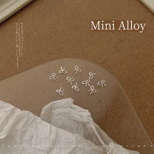 Macro shot of 4x4mm silver alloy bow nail charms scattered on textured paper background