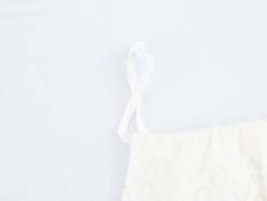 Detail of white halter neck dress featuring textured knit fabric and drawstring shoulder straps