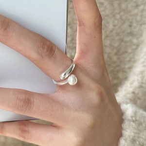 Detailed view of an open silver ring with a white pearl and metal ball on a finger