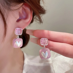 Detailed close-up of pink square earrings with a white heart pearl on silver studs