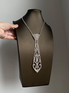 Macro view of silver tie-shaped tassel necklace with rhinestones on a black mannequin