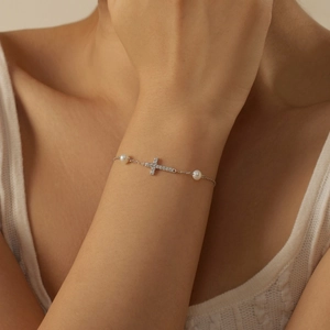 Silver cross bracelet with white pearls and diamonds worn on a woman's wrist