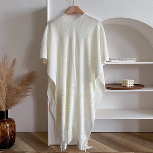 Detail of white knit shawl with fringe on hanger against a minimalist home background