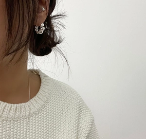 Close-up of a silver heart stud and thick hoop earring on model wearing a white knit sweater