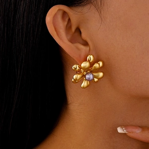 Détail de la boucle d'oreille fleur dorée mate avec perle lilas sur le mannequin