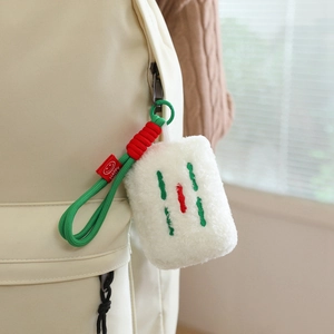 Plush mahjong keychain with embroidery hanging on a beige canvas backpack detail