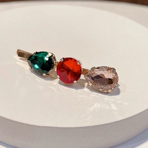 Detailed close-up of a golden hair clip featuring red, emerald and pink gemstones