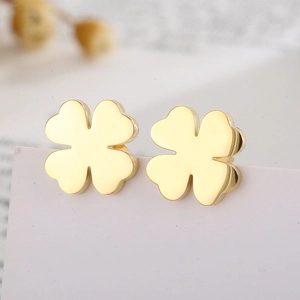 Macro shot of minimalist gold four-leaf clover stud earrings on a card edge
