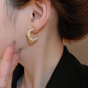 Detail view of elegant C-shaped gold-plated earrings with pearls worn on model ear