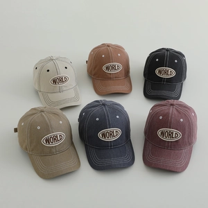 Detail view of washed denim baseball caps for kids with WORLD embroidery in six colors