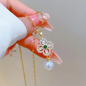 Close-up of gold clover necklace with green gemstone, small crystals, and a white pearl