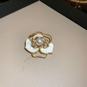 Vue macro d'une broche camélia avec pétales en nacre et une perle blanche centrale