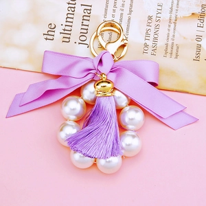 Detail view of pearl keychain with purple silk ribbon bow and golden metal hook on magazine