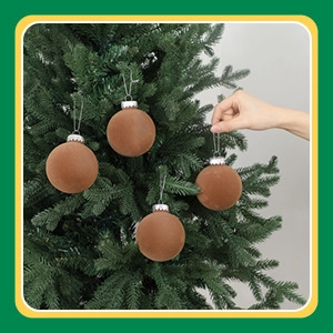 Close-up of velvet 8cm Christmas baubles in earth tones hanging on a tree with hand for scale
