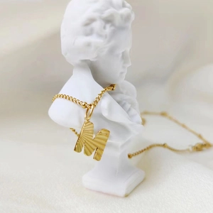 Detailed view of a gold stainless steel necklace featuring a letter M pendant on a bust