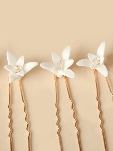 Detailed view of three white ceramic flower hair pins with crystal beads on gold-tone metal