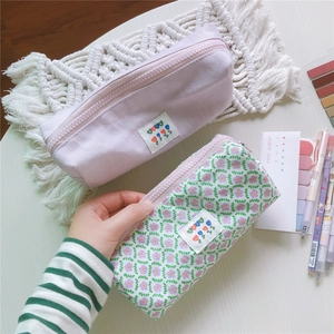 Detalle de estuches de lona en lila pastel y flores sobre escritorio de madera blanca