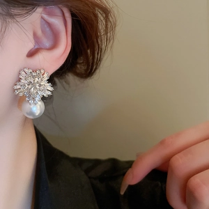 Elegant flower stud earrings with shimmering zircons and round pearls worn by a model