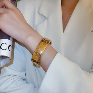 Detail of a wide gold metal bracelet featuring vintage embossed patterns on a female wrist