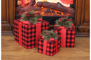 Trois boîtes cadeaux de Noël à carreaux rouges avec des pommes de pin près du feu