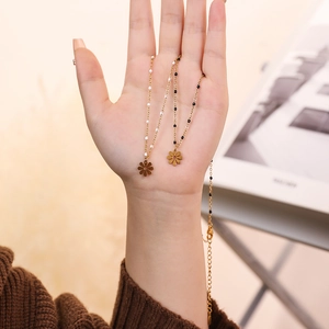 Detailed shot of two gold flower necklaces with white and black beads held in hand