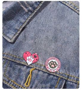 Detail of pink enamel paw badges pinned on denim jacket showing Rescue Adopt Foster text