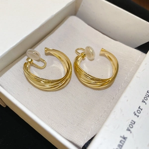 Macro shot of twisted gold circular clip-on earrings on gray velvet inside a jewelry box