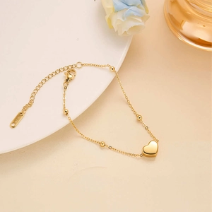 Macro detail of gold beaded heart bracelet with polished heart pendant and lobster clasp