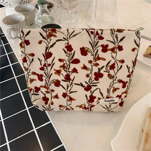 Trousse de maquillage en velours côtelé à fleurs avec étiquette Sozakka sur table