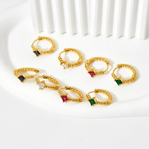 Detailed macro of gold twisted hoop earrings with emerald, black, red, and clear gems