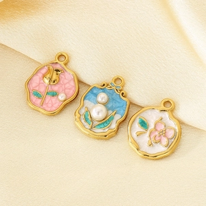 Détail de pendentifs vintage émaillés fleur et perle sur tissu en soie beige