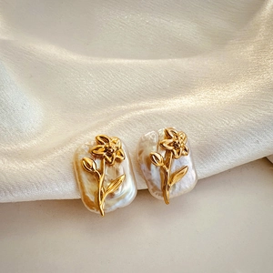 Detail of golden floral patterns on baroque pearl earrings resting on beige silk