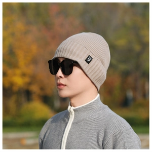 Close-up of beige ribbed knit beanie with brand logo patch on a blurred autumn background
